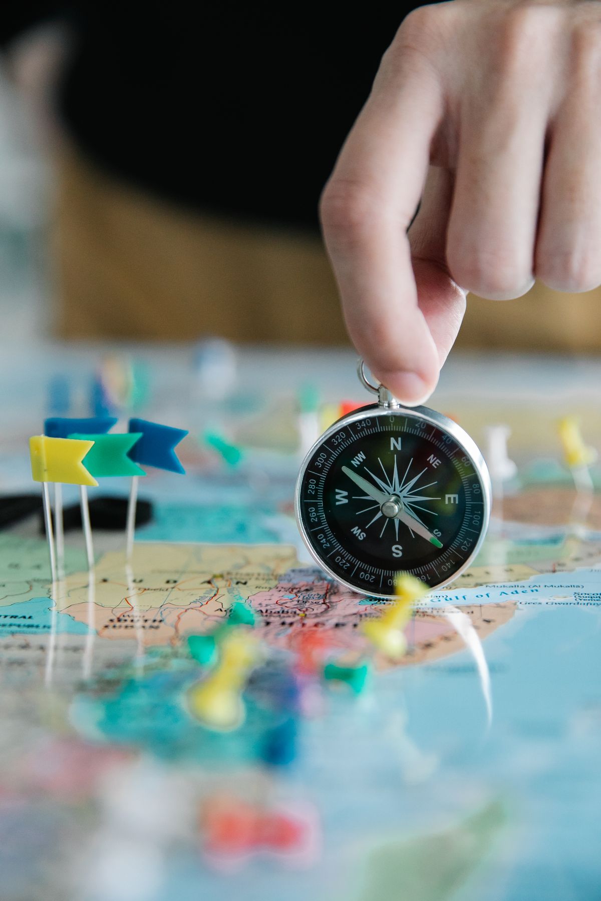 Hand holding a compass over a map marked with location pins